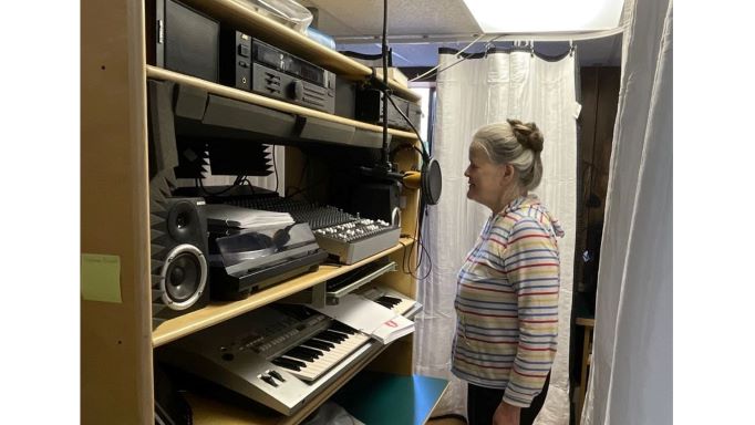 Gudrun Brunot singing into a microphone in front of a wall of music recording equipment